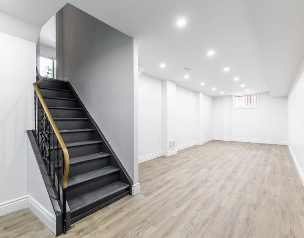 an empty basement white hardwood floors and a black staircase