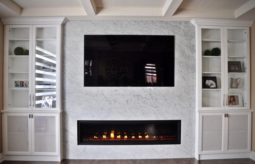 flat screen television surrounded by marble with a gas fireplace underneath